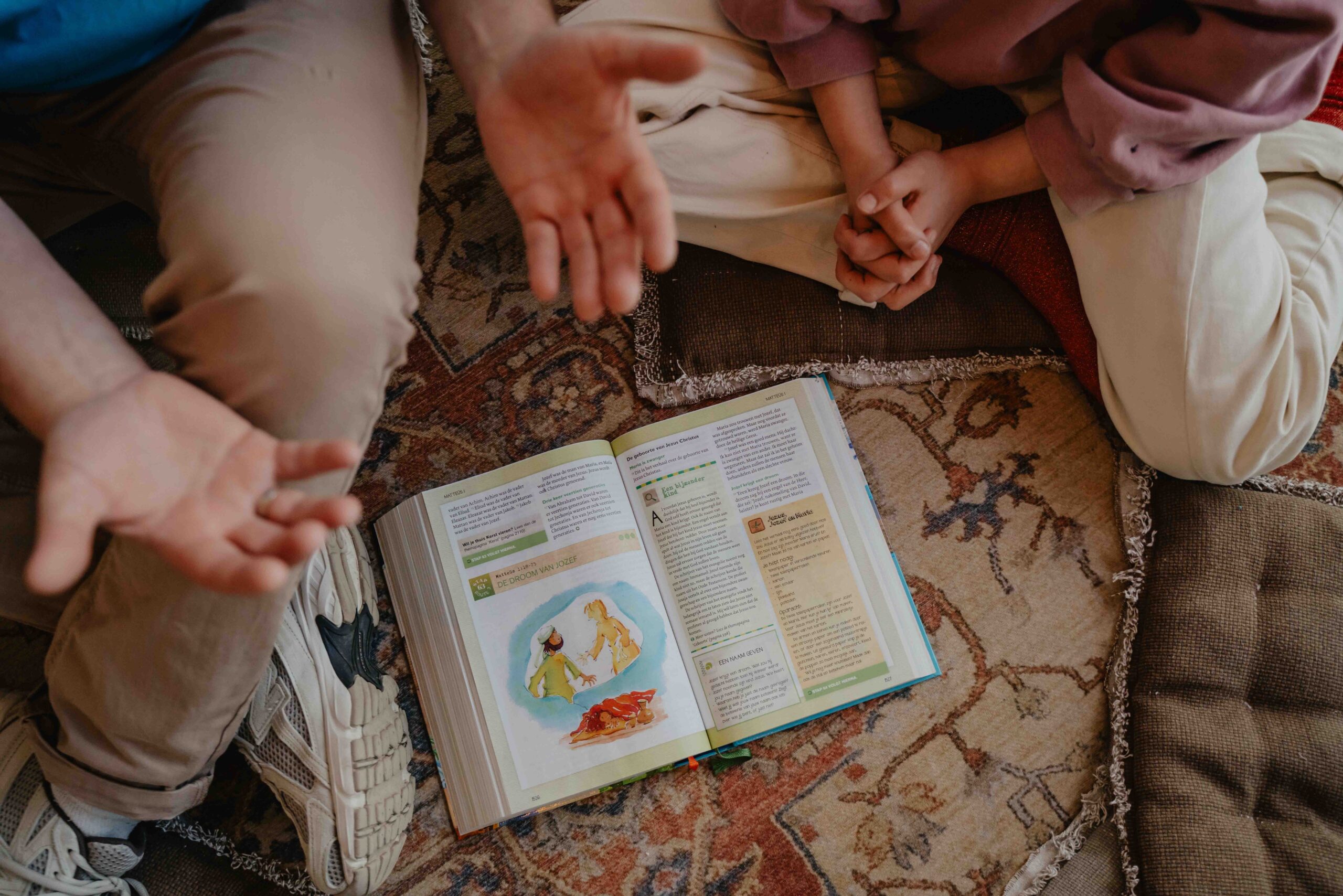 Open kinderbijbel op een kleed, met de handen van een kind en een vrijwilliger eromheen