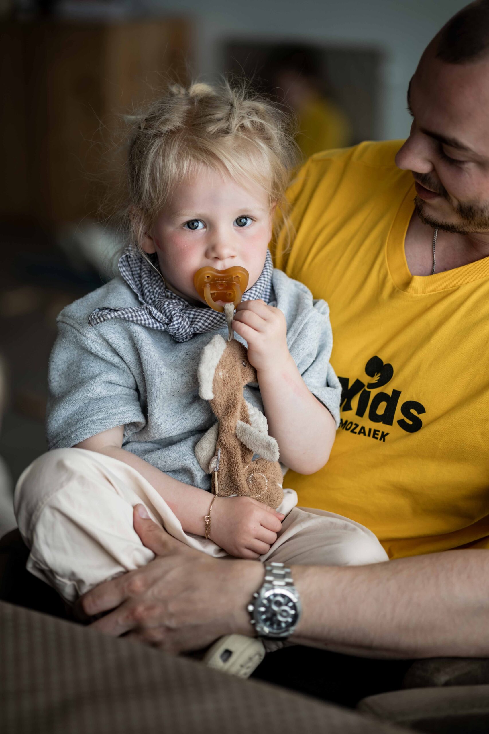Peuter met knuffel zit op schoot bij een vrijwilliger van Mozaiek Kids