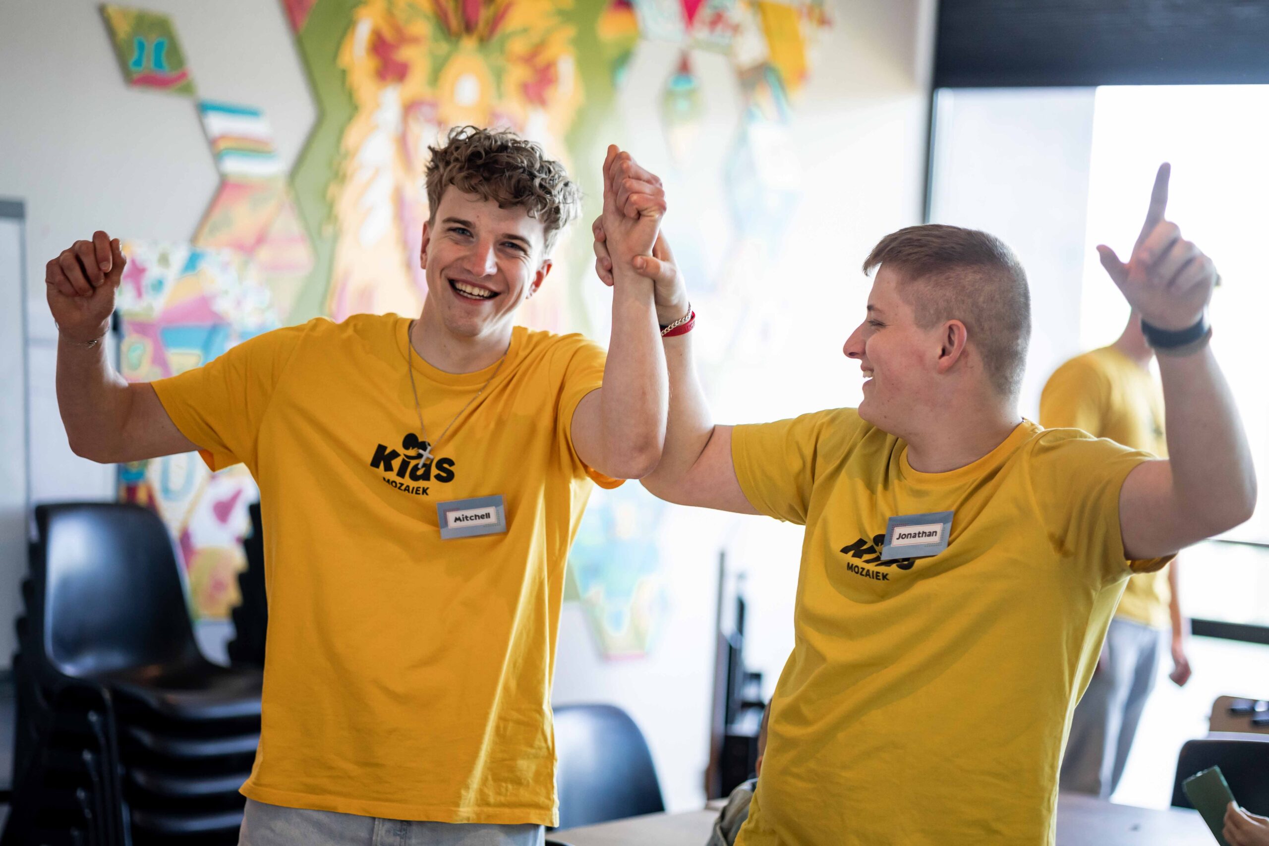 Twee vrijwilligers in gele Kids-shirts doen enthousiast mee met een spel