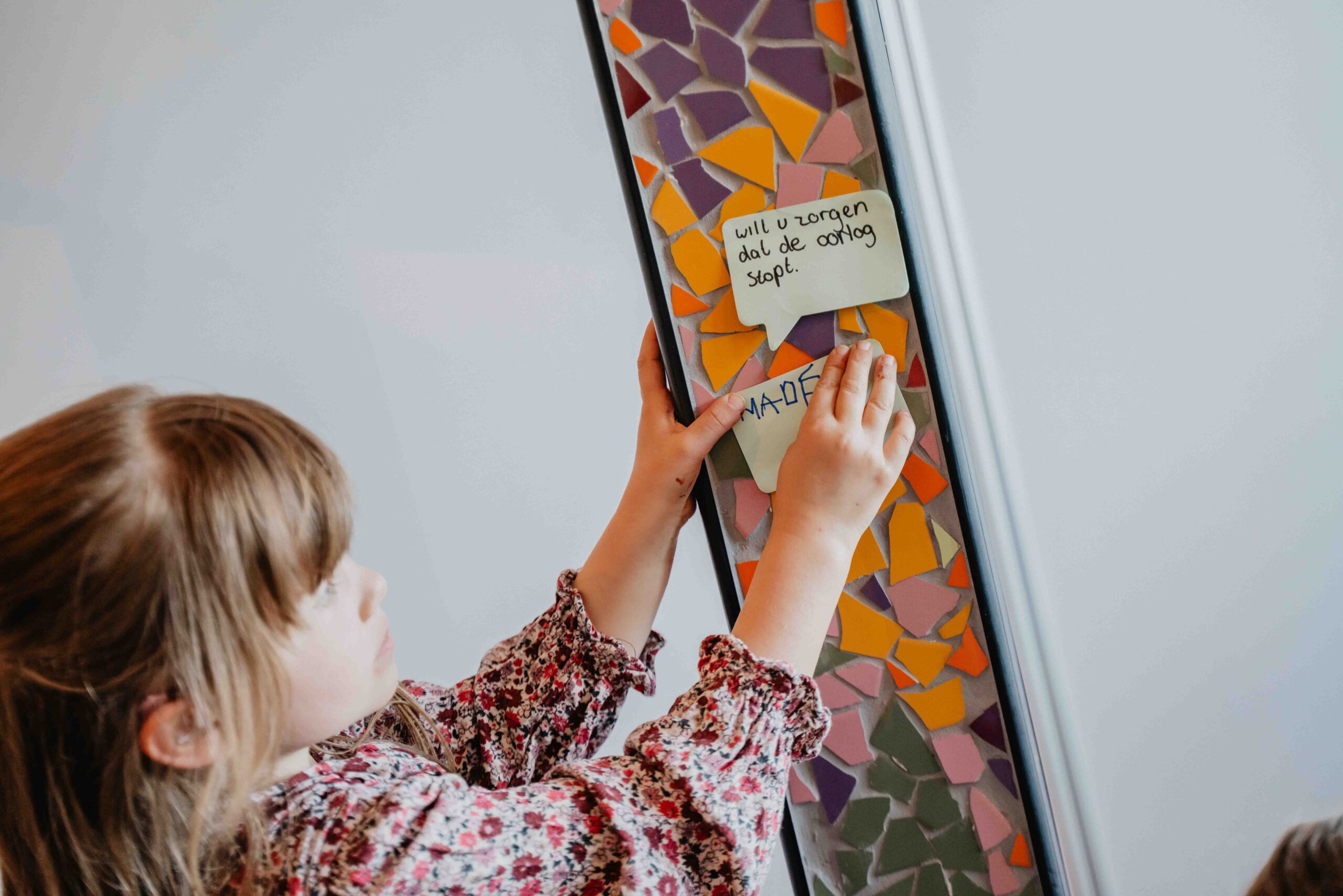 Meisje hangt een gebedsbriefje op de kleurrijke gebedsmuur in de kidszaal