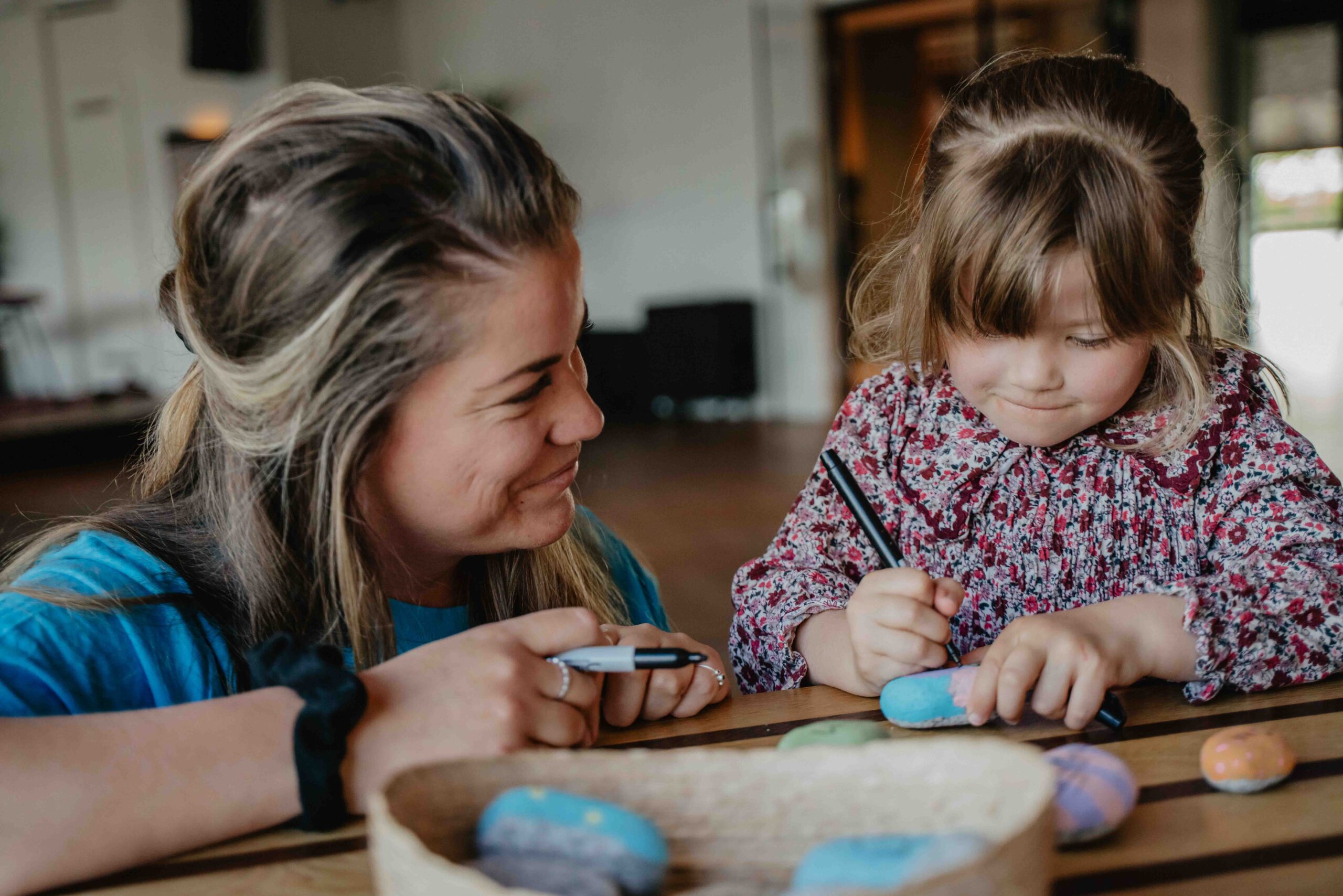 Vrijwilliger en meisje maken samen beschilderde stenen aan tafel