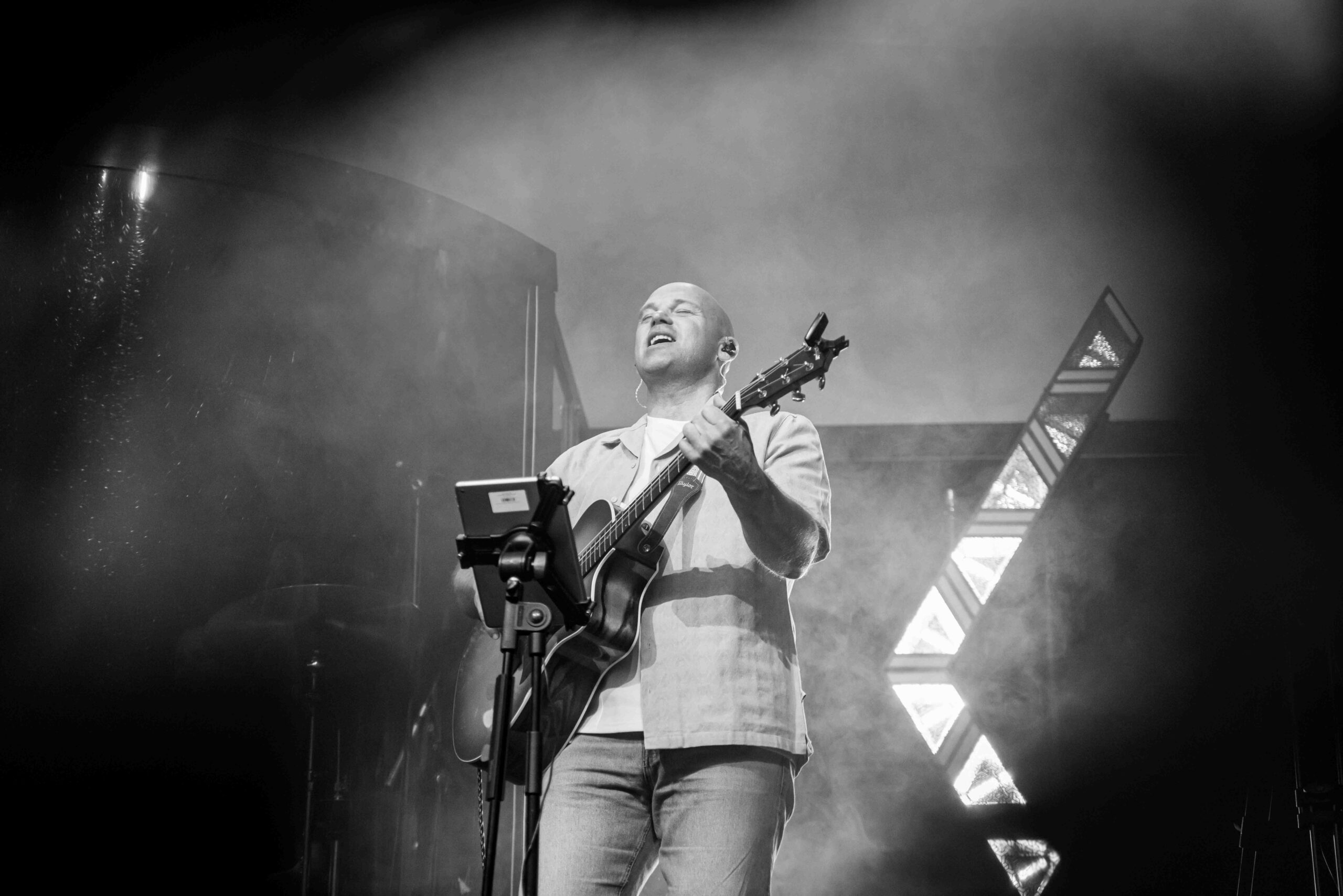 Worshipleider met akoestische gitaar zingt in rook en tegenlicht, in zwart-wit
