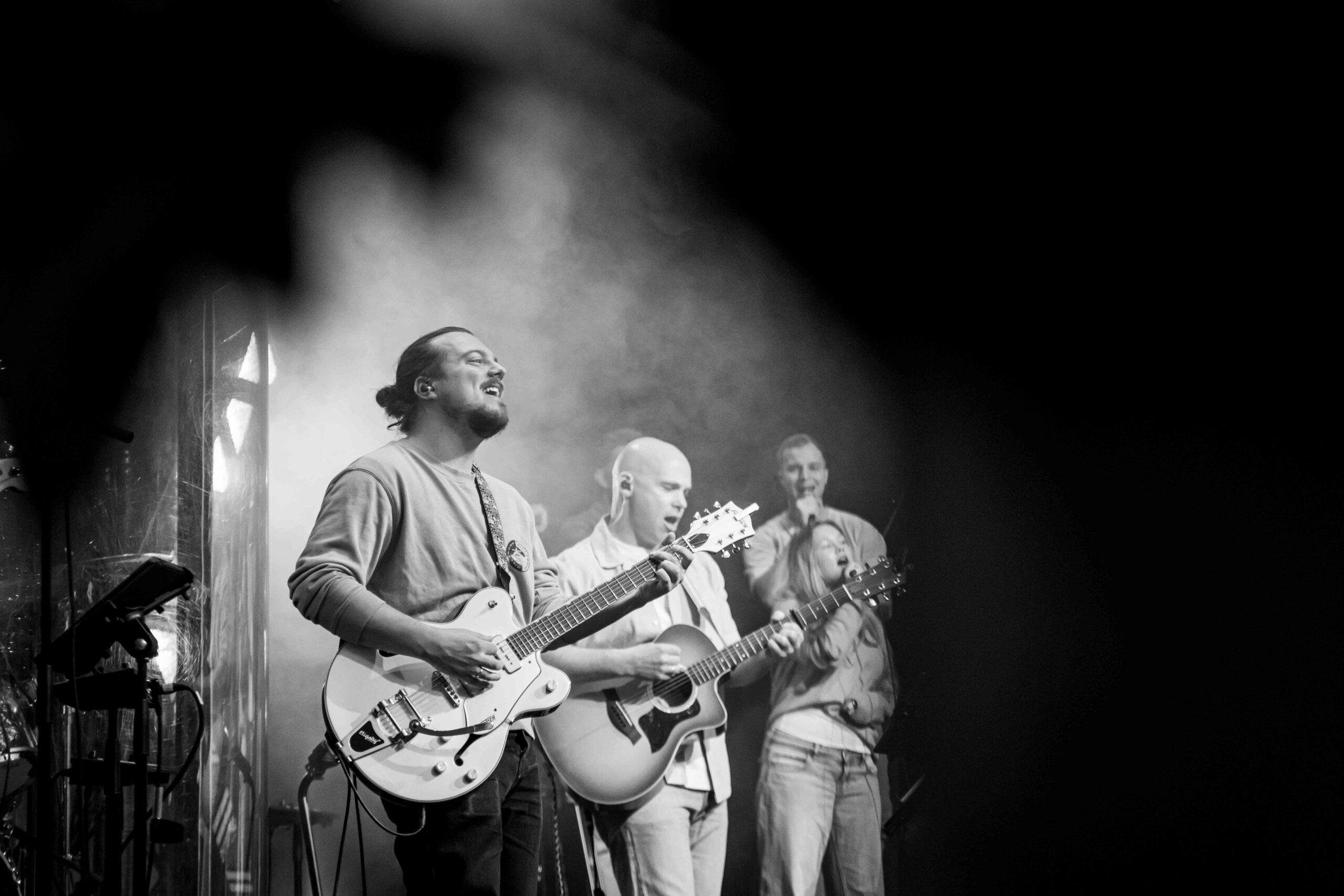 Gitaristen van de worshipband spelen op het podium, in zwart-wit