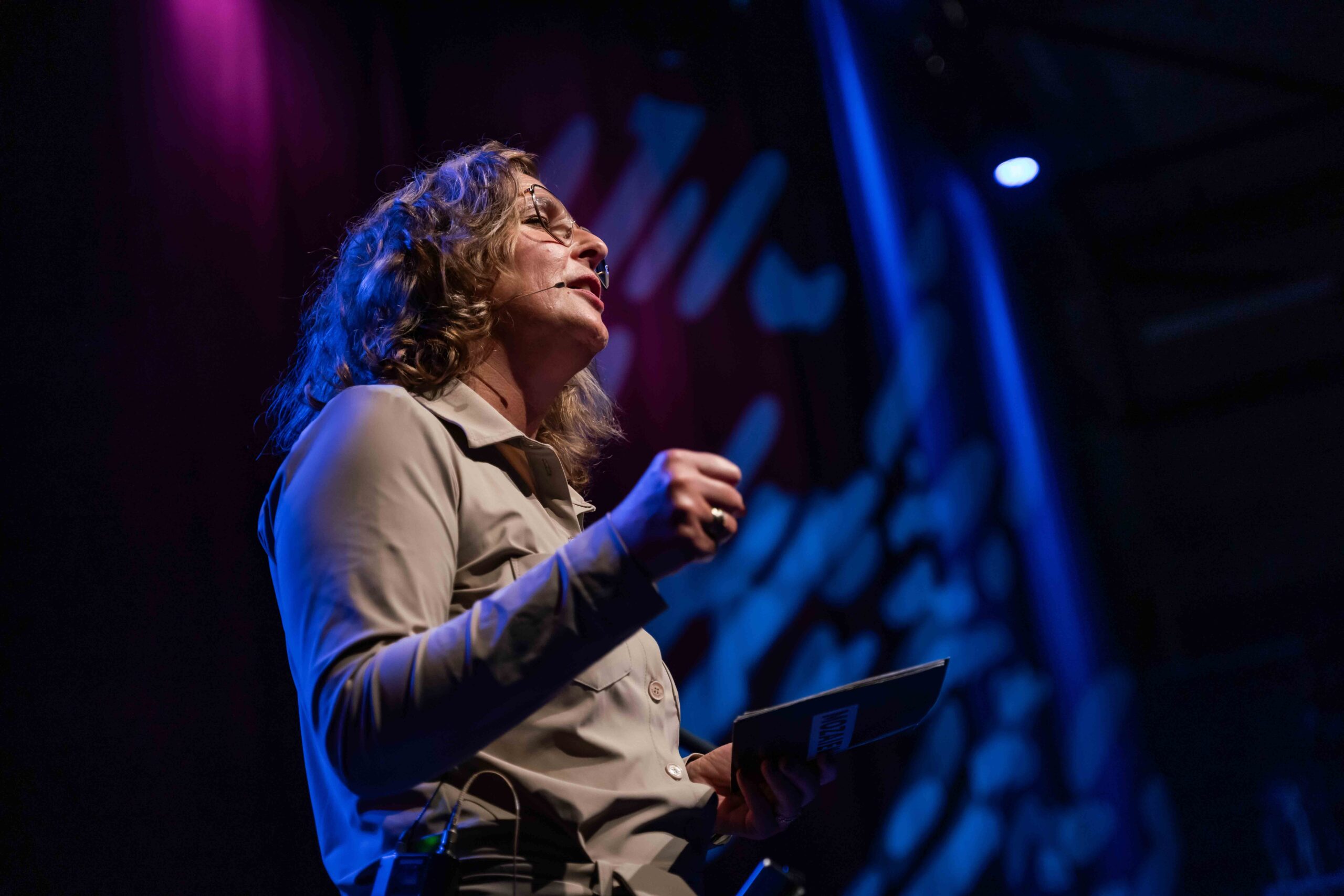 Vrouw spreekt op het podium in blauw en paars licht